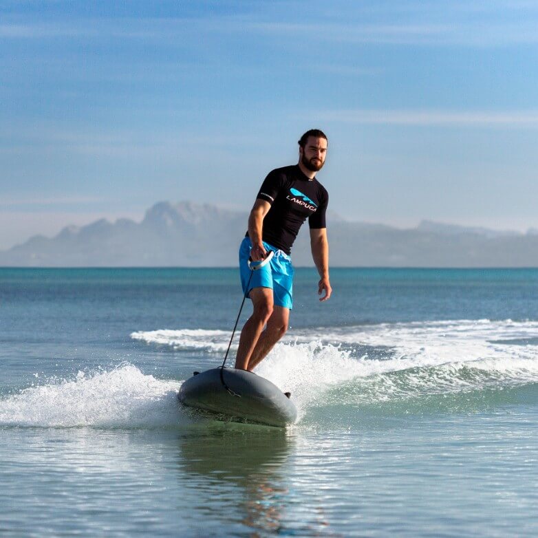 Man in a black Lampuga shirt riding on the ocean with mountains in the horizon